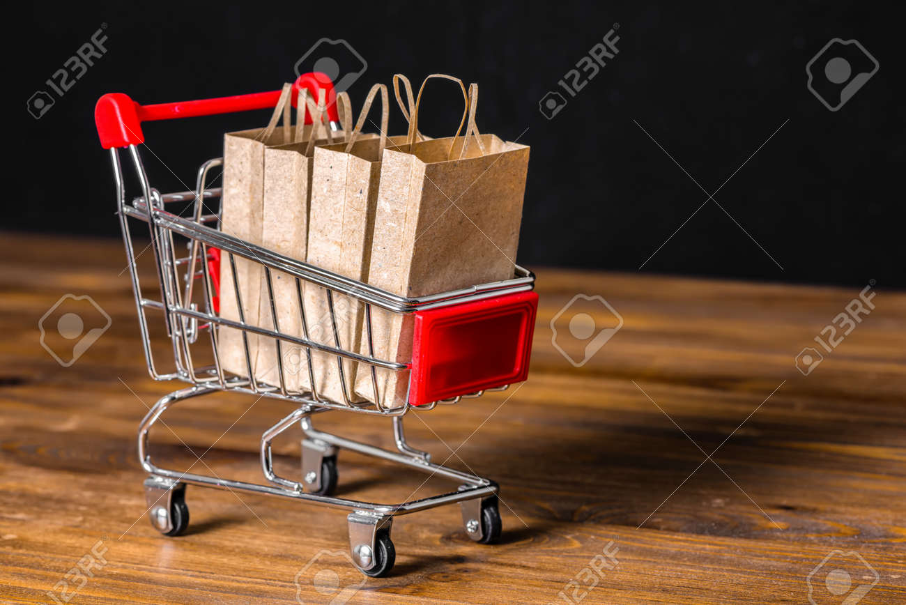 66152715-concept-of-sale-with-shopping-cart-paper-bags-on-wooden-background-over-black-close-up.jpg